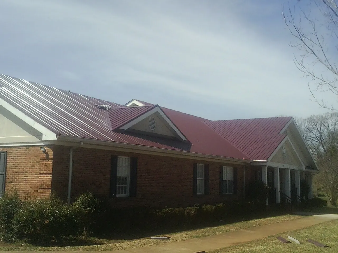 Red metal roof with gabled entries on a long brick building, from a Hail Damage Roof Repair job in Jarrell