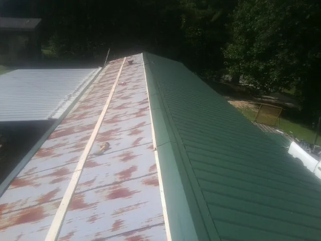 Old rusted panels beside newly installed green metal roofing — Wind Damage Roof Repair by Roofing Brothers in Jarrell